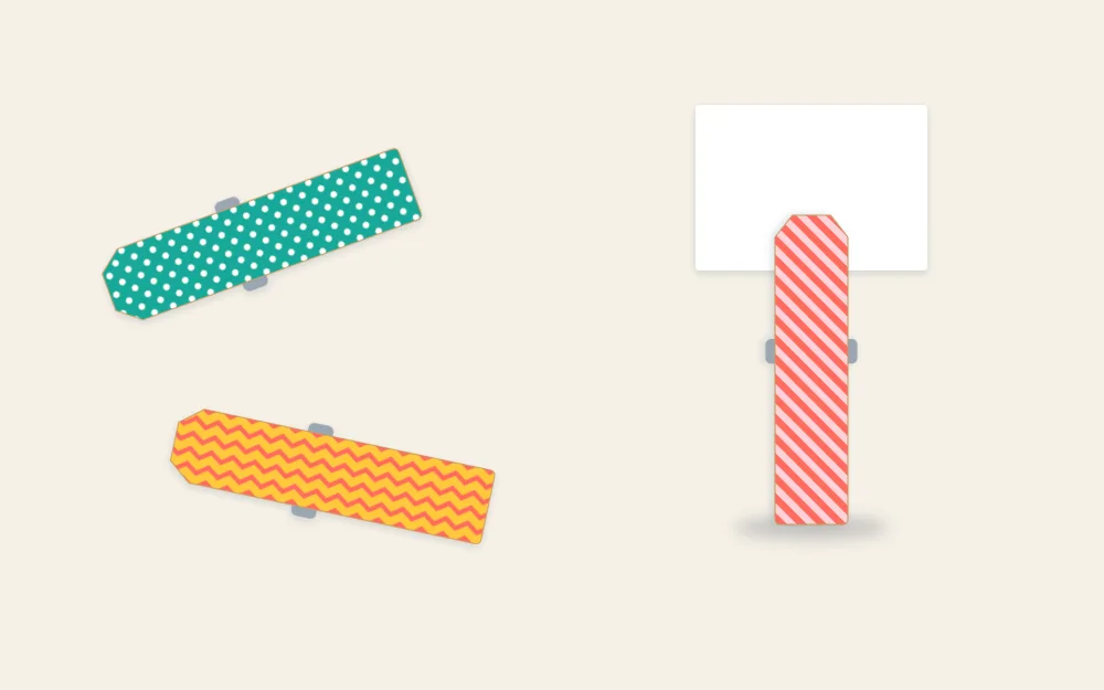 Three finished washi-covered clothespins in different patterns, one standing upright and holding a small blank card